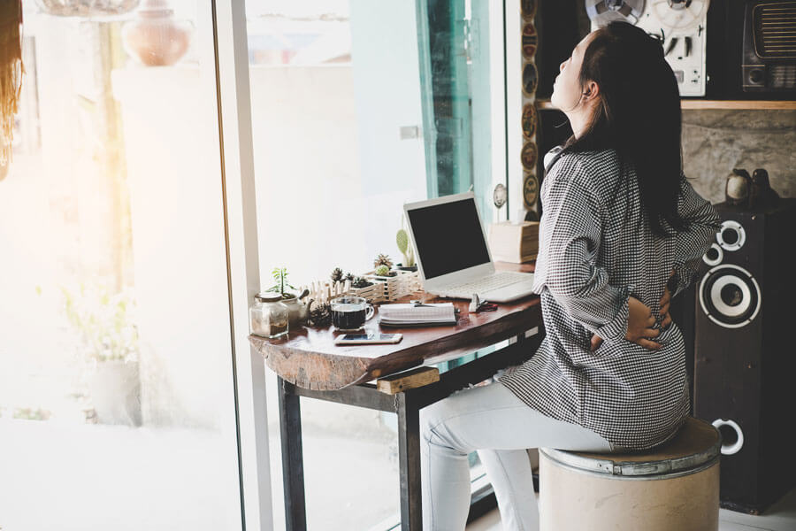 female at computer holding lower back pain